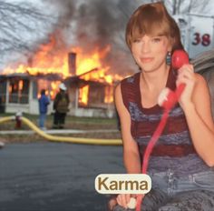 a woman holding a red hose in front of a fire that is burning behind her