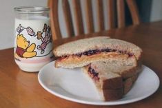 a sandwich on a plate next to a glass of milk and a winnie the pooh mug