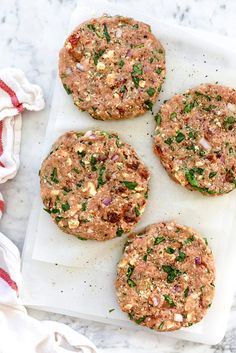 four burgers sitting on top of a white cutting board next to a red and white napkin