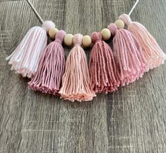 three tasselled necklaces with wooden beads on a wood surface, one in pink and the other in white