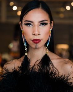 a woman with long black hair and tattoos on her face, wearing feathers around her neck