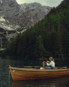 two people are sitting in a boat on the water with mountains in the back ground