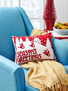 a blue chair with a red and white pillow sitting on it next to a bowl of fruit