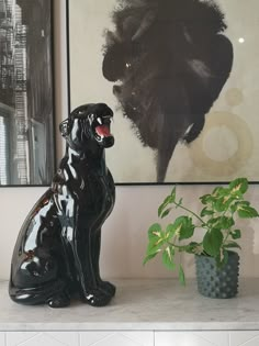 a black dog statue sitting on top of a white shelf next to a potted plant