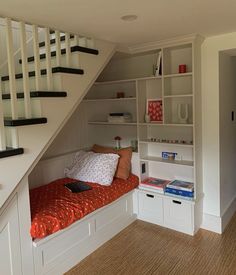 there is a small bed under the stairs in this room with bookshelves and drawers