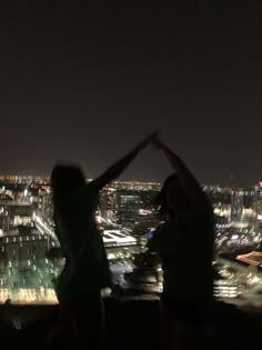 two people standing on top of a building at night with their arms in the air