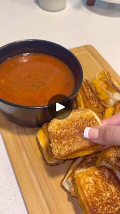 someone is dipping cheese on top of grilled sandwiches with tomato soup in the background