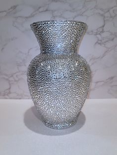 a silver vase sitting on top of a table next to a marble wall and floor