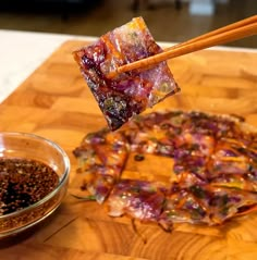 chopsticks sticking out of food sitting on top of a wooden cutting board next to a bowl