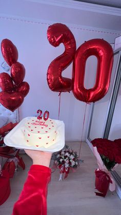 a person holding a cake with the number 20 on it and balloons in the background