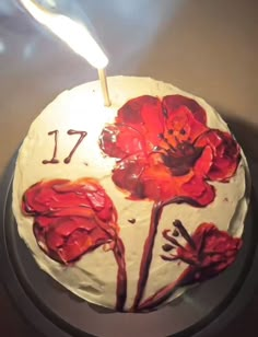 a white cake with red flowers on it and a lit candle sticking out of the top