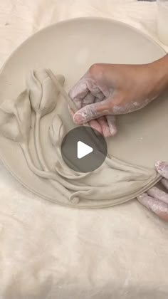 a person is making something out of clay on a white plate with one hand and the other