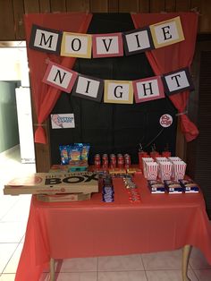 a movie night party with popcorn, sodas and snacks on a table in front of a red curtain