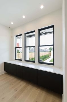 an empty room with three windows and black cabinets on the wall, along with hardwood flooring