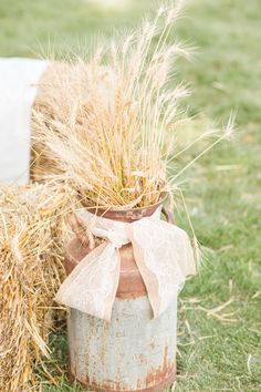 an old tin can with hay in it and a bow tied around the top is sitting on some grass