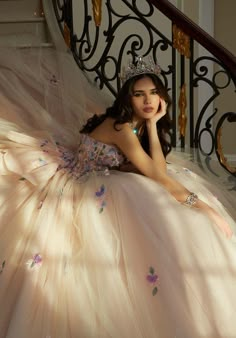 a beautiful young woman in a ball gown sitting on the stairs wearing a tiara