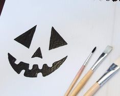 some paint brushes are sitting on top of a piece of paper with a jack - o'- lantern face