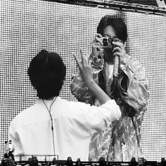 two people taking pictures with their cell phones at a music festival, one person holding up his camera to take a picture