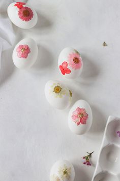 some white eggs with pink flowers painted on them next to two spoons and one is empty