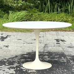 a white table sitting on top of a cement ground next to grass and bushes in the background