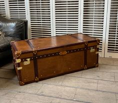 an old trunk sitting on the floor in front of a leather chair and window with shutters