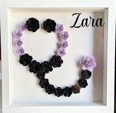 a white frame with black and purple paper flowers in the shape of a letter q