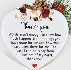 a white heart shaped plaque with the words thank you written on it, surrounded by flowers and pine cones