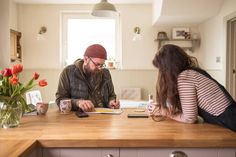 a man and woman sitting at a kitchen counter with flowers in vases on the table