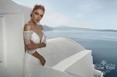 a beautiful woman in a white dress leaning against a wall near the ocean with her arms crossed