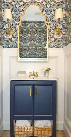 a bathroom with a blue cabinet, mirror and two lamps on the wall above it