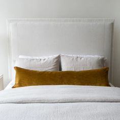 a white bed with two pillows on top of it and a headboard in the background