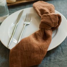 a white plate topped with a brown napkin next to a fork and knife on top of a table