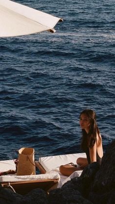 a woman sitting on the edge of a boat in the ocean next to rocks and an umbrella