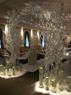 snow covered trees and vases in the middle of a room with lights hanging from the ceiling