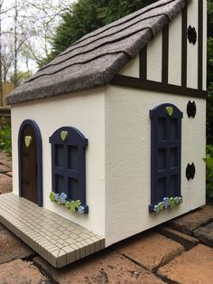 a small white house with blue windows and shutters on the outside, sitting on a brick patio