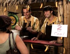 three men standing in front of a table with bananas hanging from it's ceiling