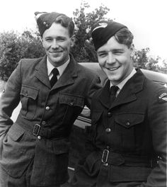 two men in uniforms standing next to each other near a car and smiling at the camera