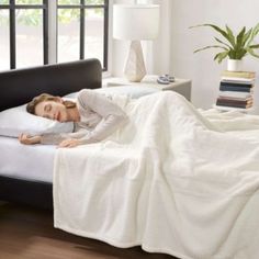 a woman laying on top of a bed under a white blanket next to a window