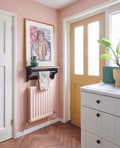 a room with pink walls and wooden floors has a painting on the radiator