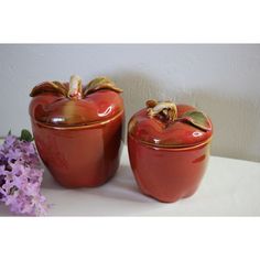 two red apple shaped containers sitting next to each other on a white table with purple flowers