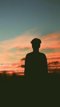 the silhouette of a man standing in front of an orange and blue sky at sunset