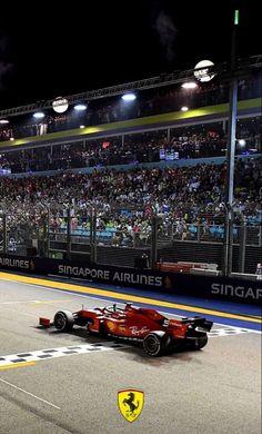 a red race car driving down the track in front of an audience at night time