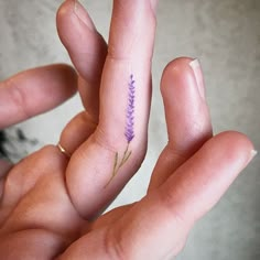 a person's hand with a tiny purple flower tattoo on their thumb and finger