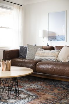 a brown leather couch sitting in a living room next to a coffee table and lamp