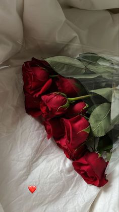 a bunch of red roses laying on top of a white sheet with a heart in the middle