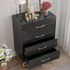 a black dresser with three drawers next to a vase filled with flowers and two candles