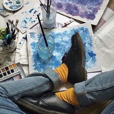 a person with their feet up on a table covered in art supplies and watercolors