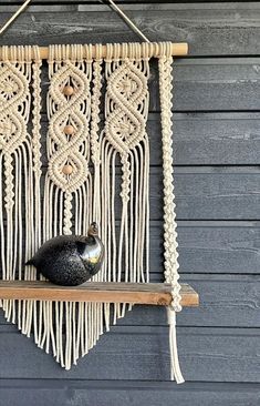 a macrame wall hanging with a black vase on it and a wooden shelf