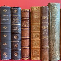 several old books lined up on a red surface with one being an orange and the other is blue