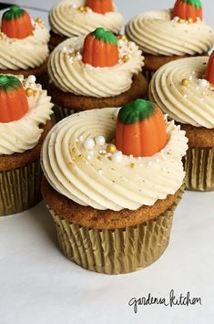 cupcakes with white frosting and pumpkin decorations on top are arranged in rows